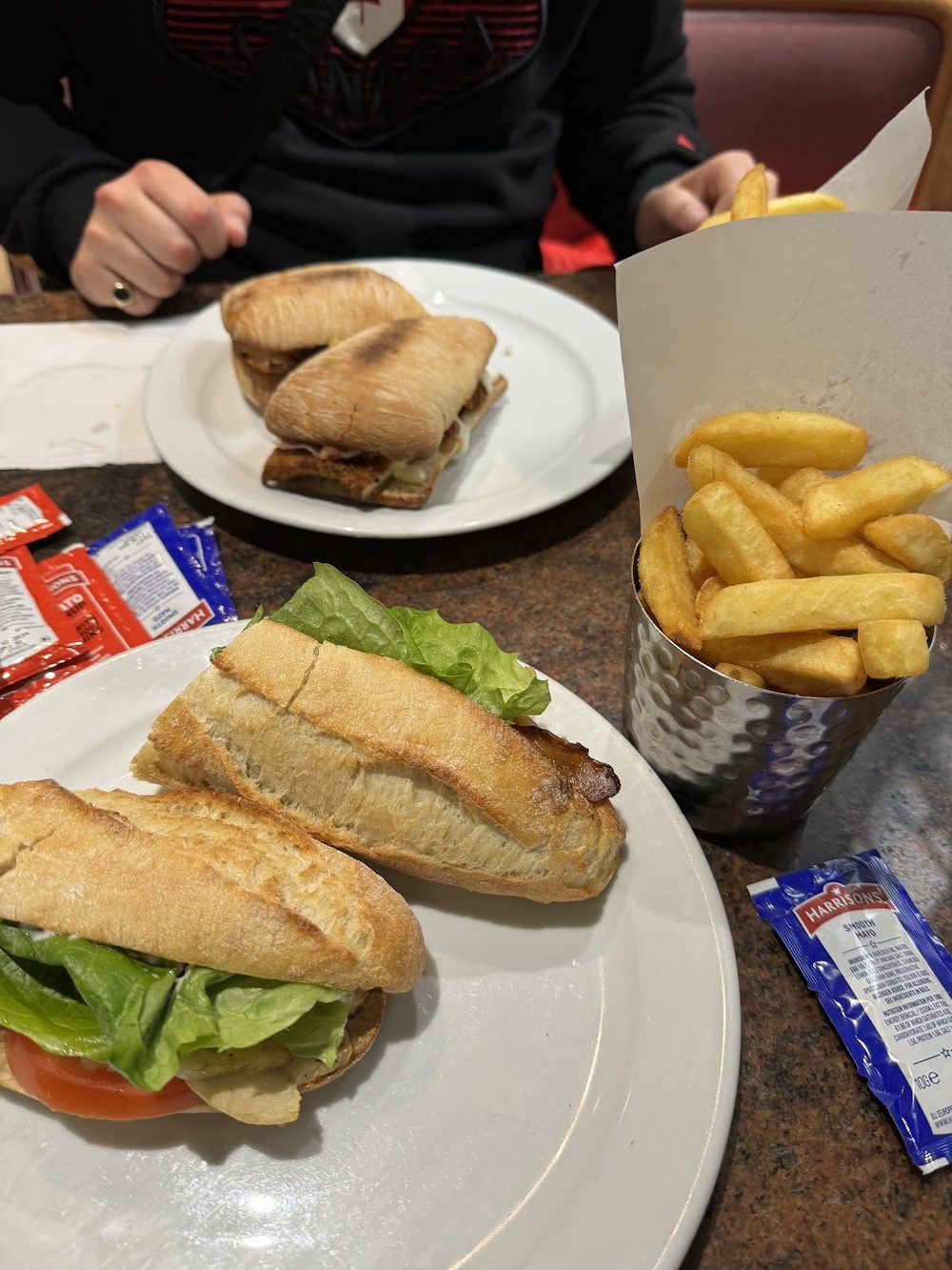 A table laid with two baguette sandwiches and a metal cup of chips