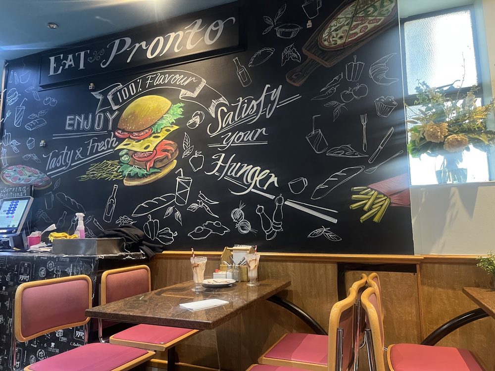 Inside El Pronto Caffe: hand-drawn chalkboard mural wall above pink booth seating and wood panelling